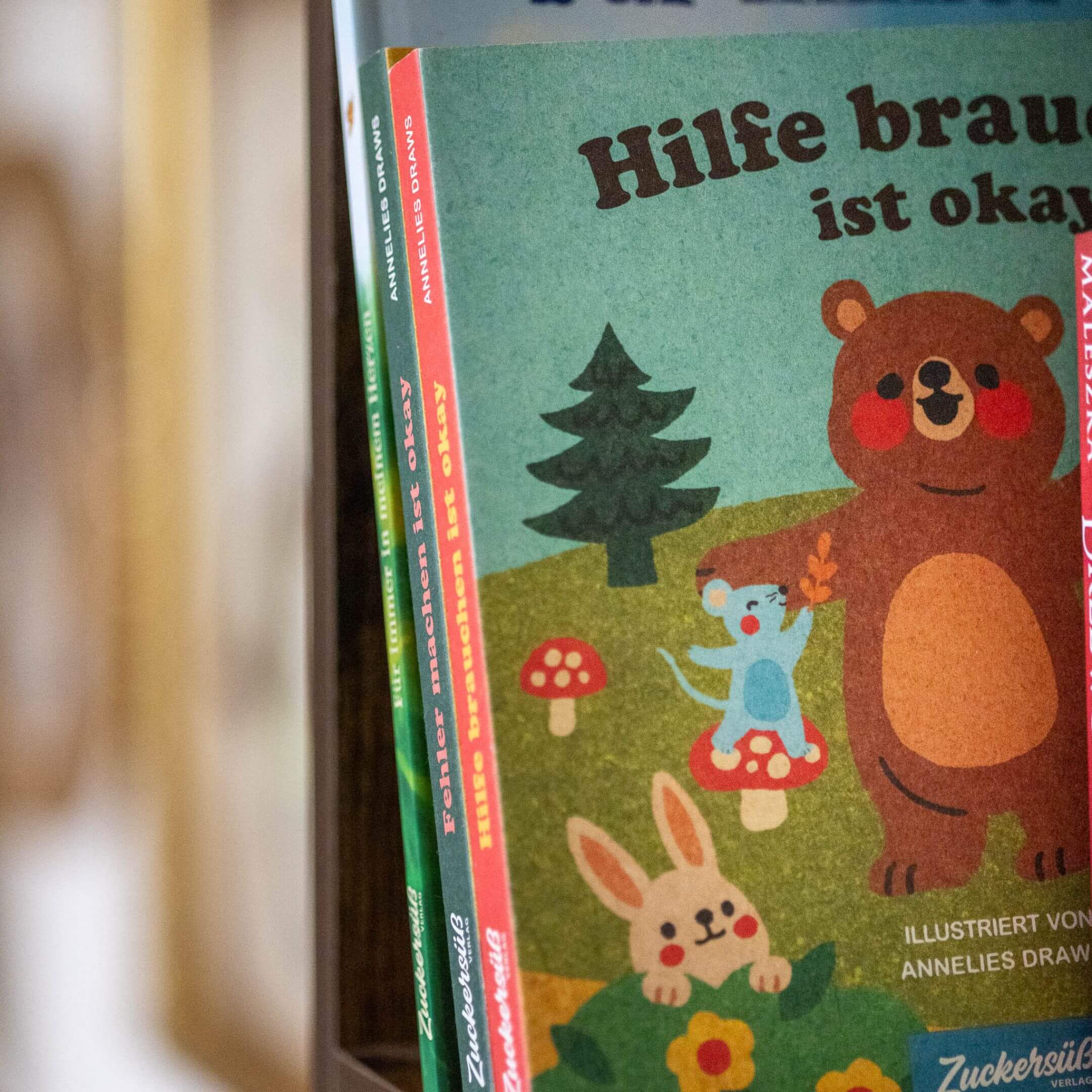 Eine Nahaufnahme von "Hilfe brauchen ist ok" von Annelies Draws, einem farbenfrohen deutschen Kinderbuch mit einem lächelnden Bären, einer blauen Maus, einem Hasen und roten Pilzen auf dem Cover, die für Freundschaft und Empathie werben.